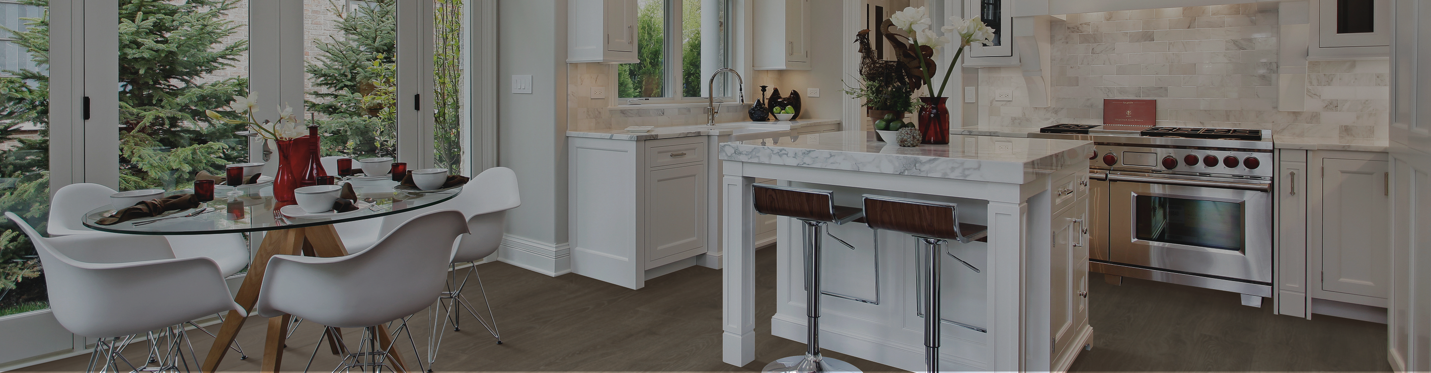 modern kitchen with white island and bar stools, stainless oven with white tile backsplash, and a round dining table by large windows with chairs and greenery visible outside.
